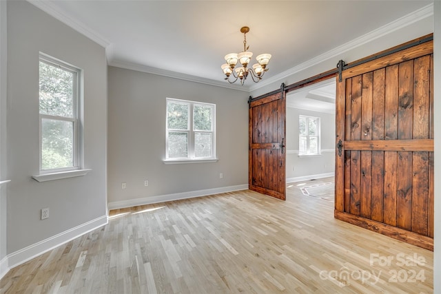 empty room featuring an inviting chandelier, a barn door, light hardwood / wood-style floors, and crown molding