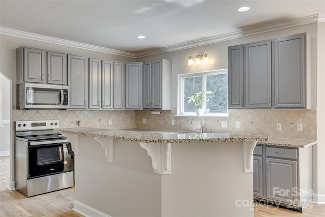 kitchen with stainless steel appliances, light stone countertops, ornamental molding, light hardwood / wood-style floors, and gray cabinetry