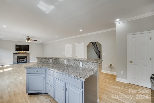 kitchen with a tiled fireplace, ceiling fan, ornamental molding, light hardwood / wood-style flooring, and light stone counters