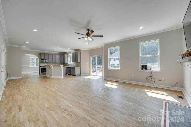 unfurnished living room with ceiling fan, light wood-type flooring, a healthy amount of sunlight, and crown molding