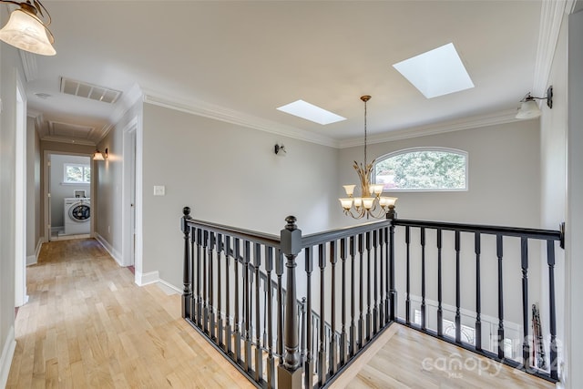 corridor with an inviting chandelier, light hardwood / wood-style floors, washer / clothes dryer, a skylight, and ornamental molding