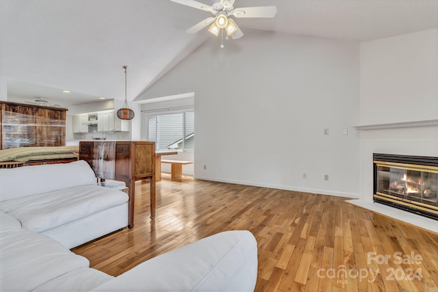 living area featuring light wood-type flooring, a fireplace with flush hearth, and a ceiling fan