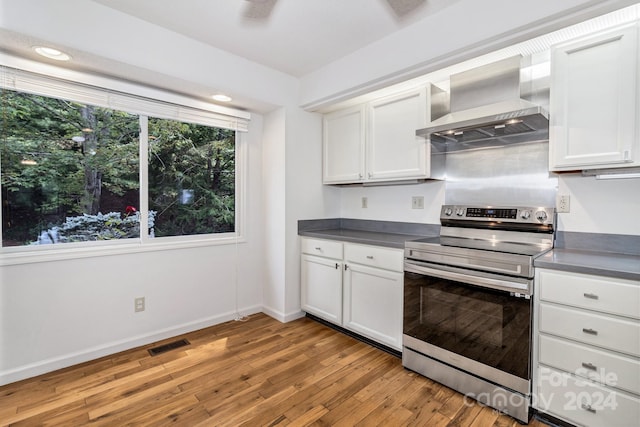 kitchen featuring dark countertops, wall chimney exhaust hood, stainless steel electric range, light wood-type flooring, and white cabinetry