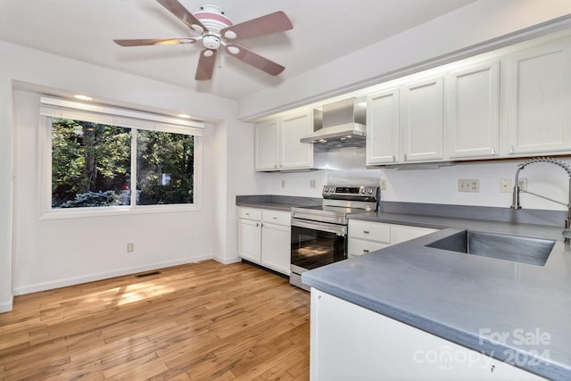 kitchen featuring electric range, white cabinets, dark countertops, wall chimney exhaust hood, and a sink