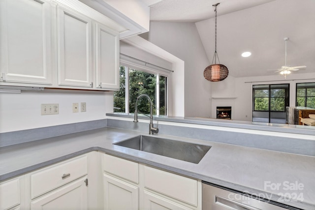 kitchen featuring a warm lit fireplace, hanging light fixtures, a sink, white cabinetry, and stainless steel dishwasher