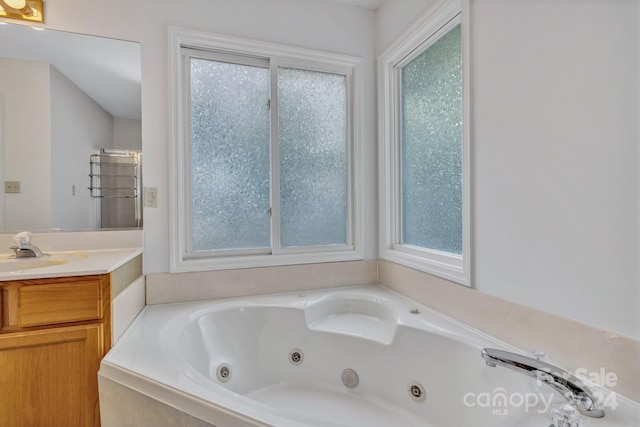 bathroom with a tub with jets, vanity, and a wealth of natural light