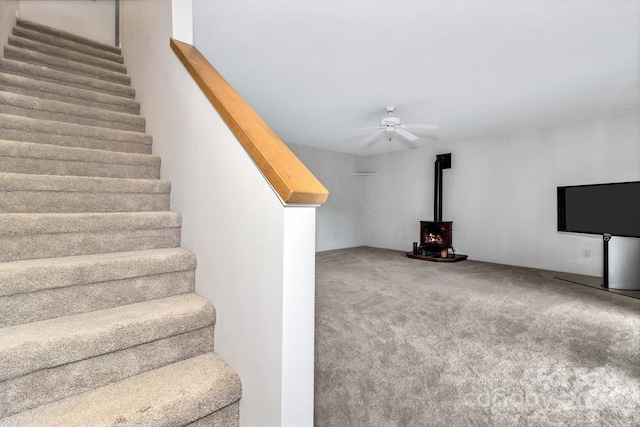 stairway with carpet, a wood stove, and ceiling fan