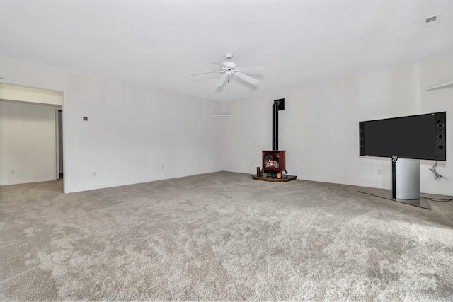 unfurnished living room with a wood stove, carpet, visible vents, and a ceiling fan