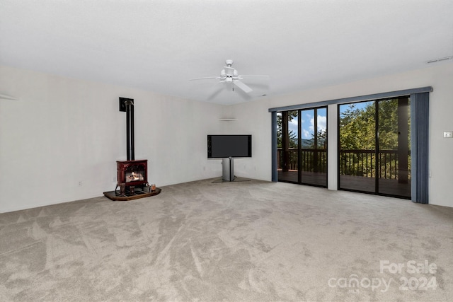 unfurnished living room featuring a wood stove, light carpet, and ceiling fan