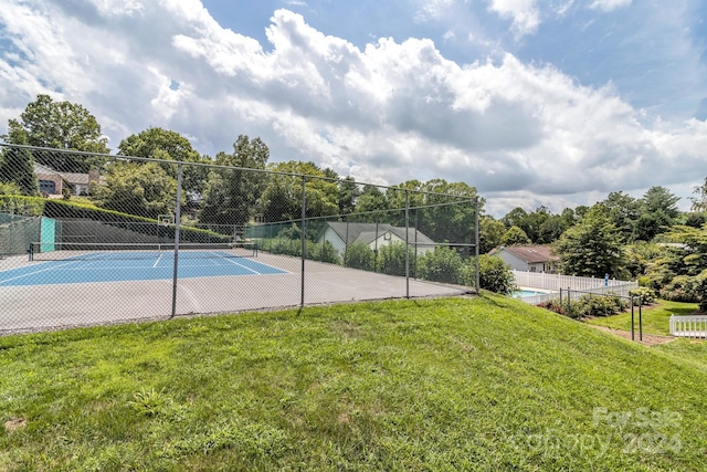 view of tennis court featuring a lawn and fence