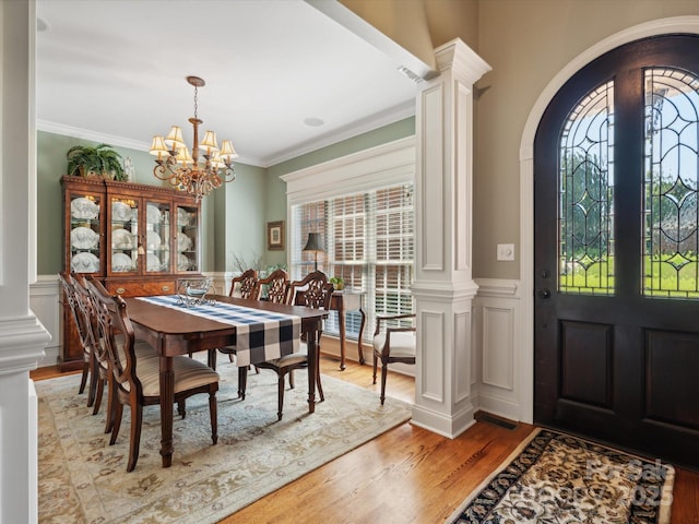 dining space with a notable chandelier, light wood-type flooring, ornamental molding, and ornate columns