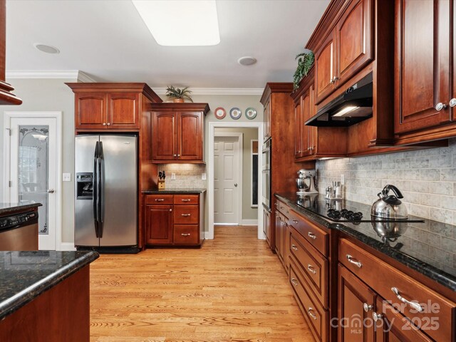 kitchen with light wood-type flooring, ornamental molding, appliances with stainless steel finishes, and dark stone counters