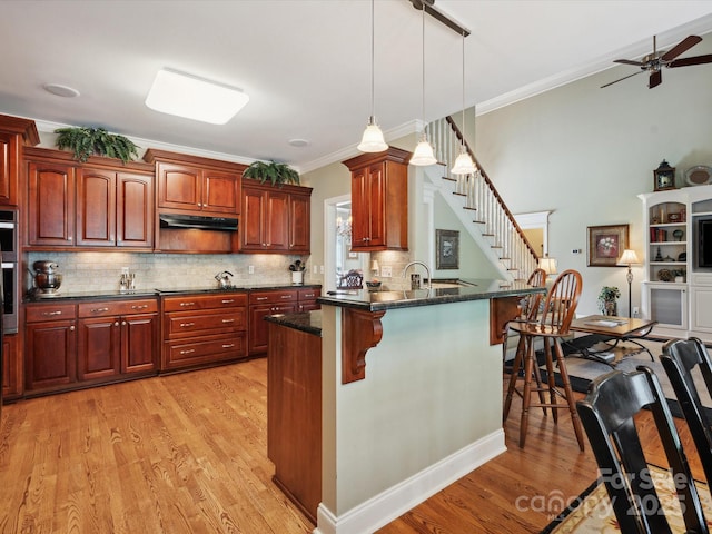 kitchen with backsplash, dark stone countertops, crown molding, pendant lighting, and light wood-type flooring