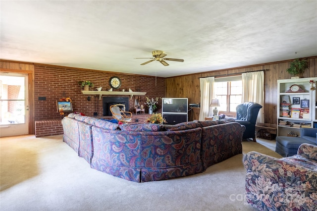 carpeted living room featuring wood walls, ceiling fan, a fireplace, and brick wall