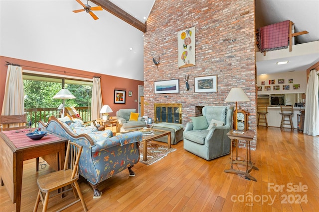 living room featuring ceiling fan, light wood-type flooring, brick wall, high vaulted ceiling, and a brick fireplace