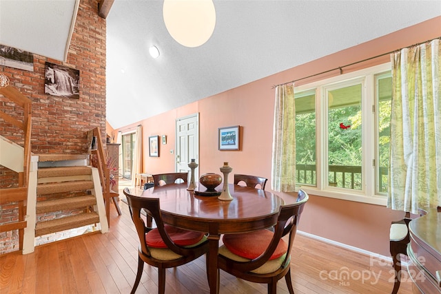 dining space with a textured ceiling, light hardwood / wood-style flooring, and vaulted ceiling