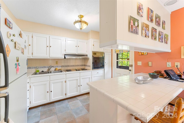 kitchen with stainless steel oven, electric cooktop, tile countertops, and white cabinets