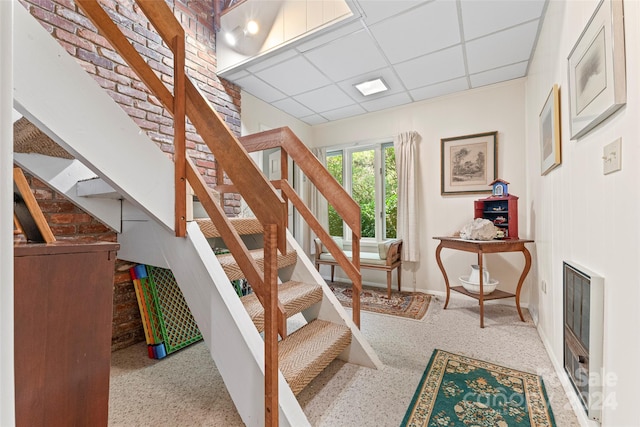 stairway with a paneled ceiling and brick wall