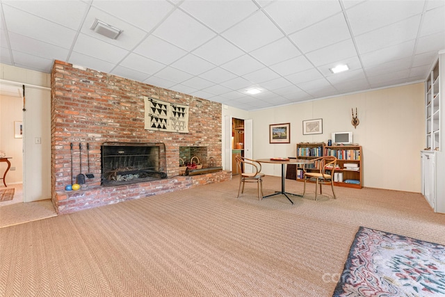 carpeted living room featuring a fireplace and a drop ceiling