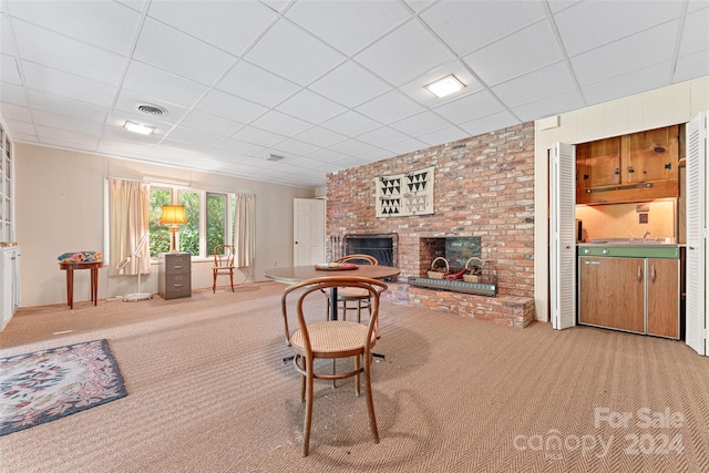 carpeted living room with a drop ceiling, brick wall, and a brick fireplace