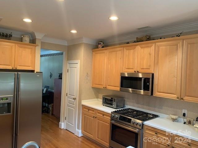 kitchen with light brown cabinets, appliances with stainless steel finishes, ornamental molding, and light hardwood / wood-style flooring