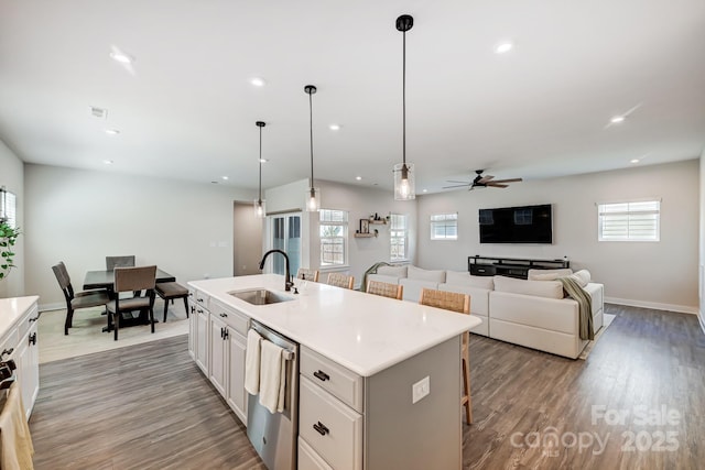 kitchen with sink, stainless steel dishwasher, decorative light fixtures, a kitchen bar, and a kitchen island with sink