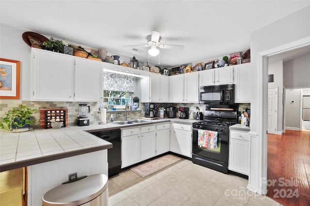 kitchen featuring light hardwood / wood-style flooring, tile counters, white cabinetry, sink, and black appliances