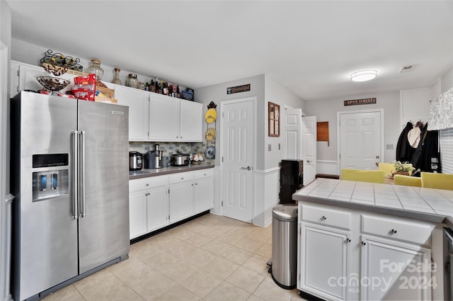 kitchen with high end refrigerator, backsplash, light tile patterned flooring, tile counters, and white cabinets