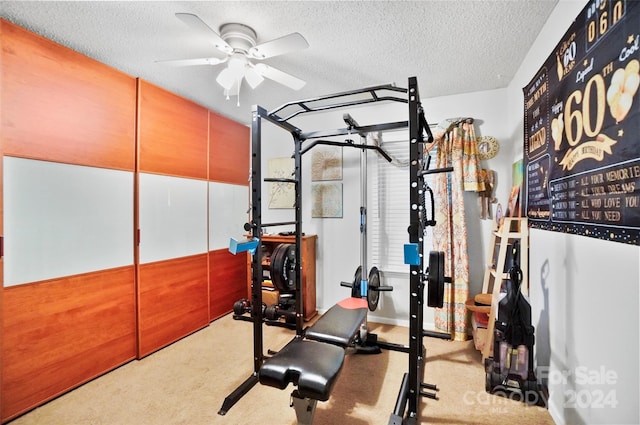 workout area featuring ceiling fan, light carpet, and a textured ceiling