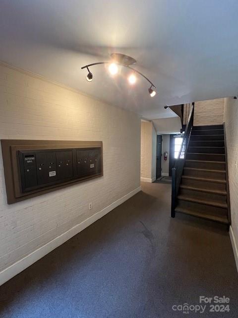 basement with carpet floors, stairway, mail area, brick wall, and baseboards