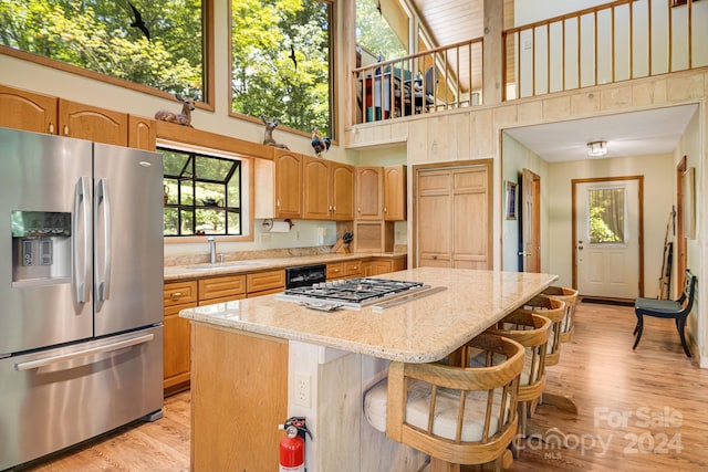 kitchen featuring appliances with stainless steel finishes, a high ceiling, a kitchen island, and light wood-type flooring