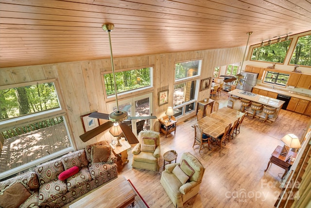 living room with a wealth of natural light, high vaulted ceiling, wood walls, and hardwood / wood-style floors