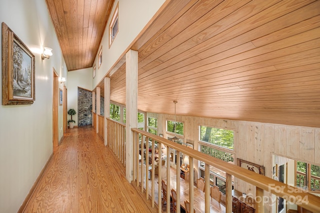 hall with high vaulted ceiling, wood walls, light hardwood / wood-style floors, and wooden ceiling