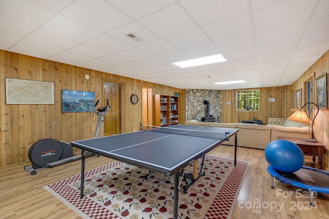 playroom with wood walls, a paneled ceiling, a wood stove, and light wood-type flooring