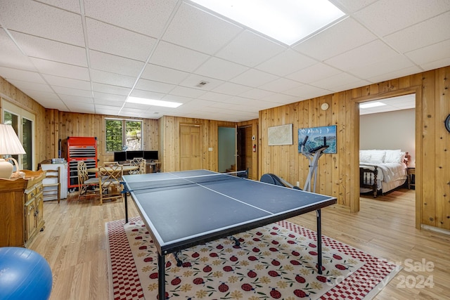 rec room with light wood-type flooring, a drop ceiling, and wood walls