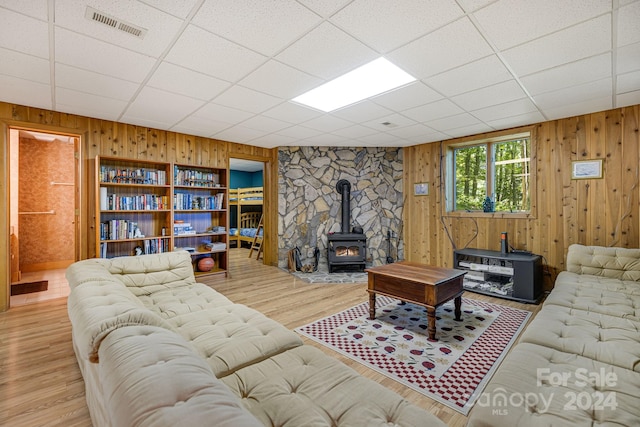 living room featuring wooden walls, light hardwood / wood-style flooring, a paneled ceiling, and a wood stove