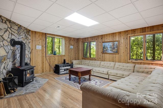 living room featuring a paneled ceiling, wooden walls, a wood stove, and light hardwood / wood-style flooring