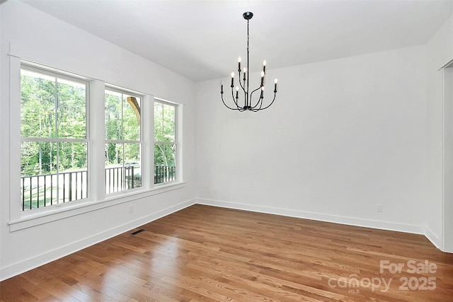 unfurnished room with hardwood / wood-style floors and a notable chandelier