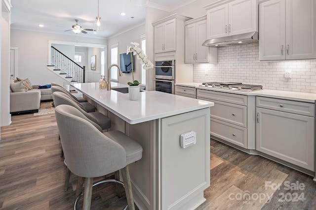 kitchen with appliances with stainless steel finishes, ceiling fan, a kitchen island with sink, and dark hardwood / wood-style flooring