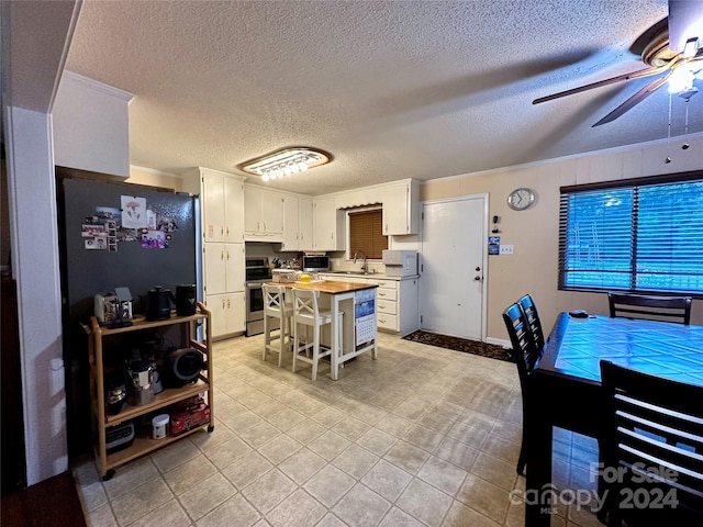 interior space with a textured ceiling, ceiling fan, appliances with stainless steel finishes, a breakfast bar area, and white cabinets