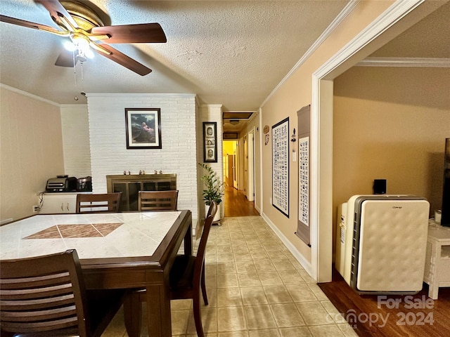 dining space with light tile patterned floors, a fireplace, a textured ceiling, ceiling fan, and ornamental molding