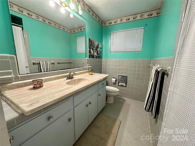 bathroom with a textured ceiling, vanity, tile patterned flooring, tile walls, and toilet