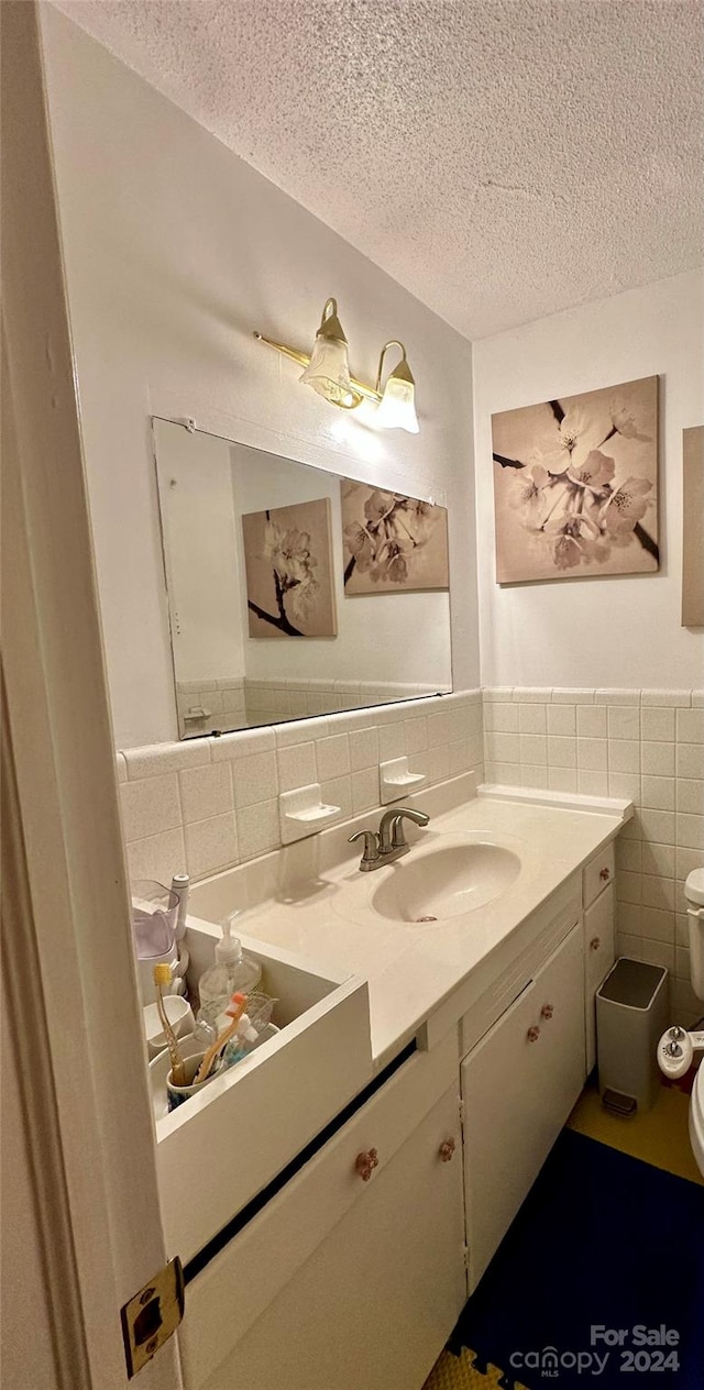 bathroom with toilet, vanity, a textured ceiling, decorative backsplash, and tile walls