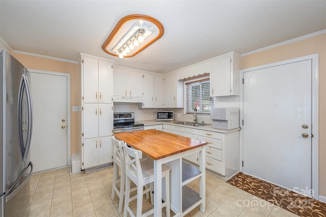 kitchen featuring white cabinetry, butcher block countertops, freestanding refrigerator, and a sink