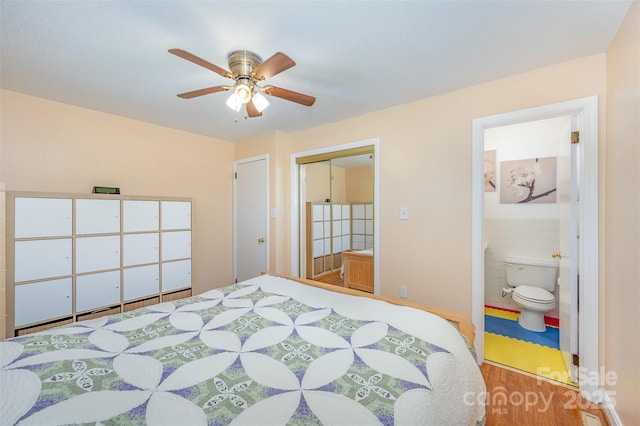 bedroom featuring connected bathroom, wood finished floors, a closet, tile walls, and a ceiling fan