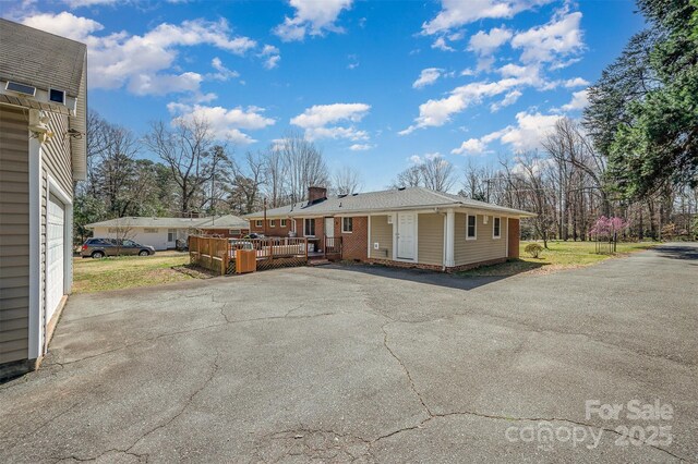 exterior space with aphalt driveway, a chimney, and a deck