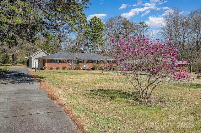 ranch-style home with aphalt driveway, brick siding, an attached garage, and a front yard