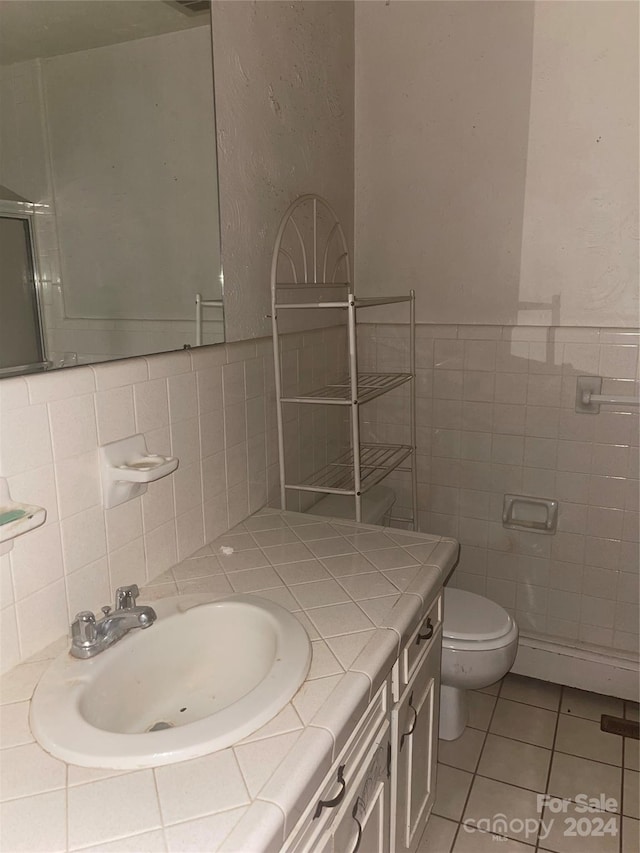 bathroom with toilet, tile patterned flooring, an enclosed shower, vanity, and tile walls