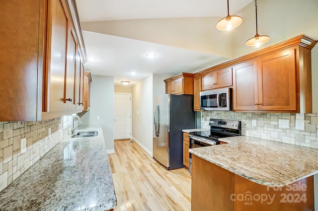 kitchen featuring kitchen peninsula, stainless steel appliances, light stone countertops, sink, and pendant lighting