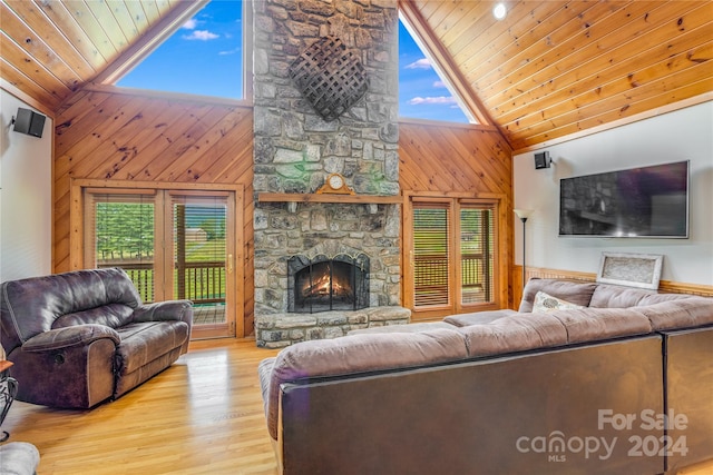 living room featuring wood walls, high vaulted ceiling, a stone fireplace, light hardwood / wood-style floors, and wood ceiling